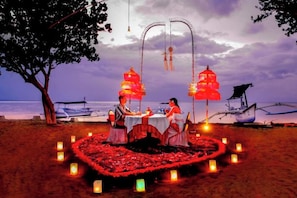 A beachside dining setup with a heart-shaped flower arrangement, a boat, and a tree.