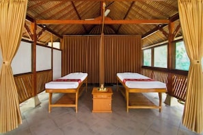 A room with two beds, a small wooden table, and a thatched roof.