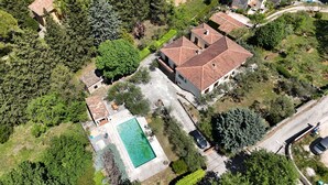 An aerial view of a residential area with a large house featuring a tiled roof, a swimming pool, and surrounding greenery.