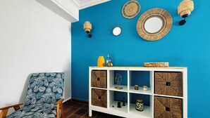 A room with a blue wall, a wooden chair with a leaf pattern, a white console table with woven shelves, and wall-mounted decorative items.