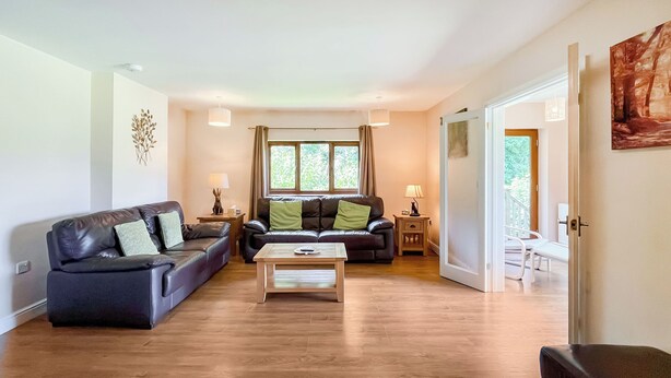 A spacious living room with a dark leather sofa, a wooden coffee table, and a view of a balcony through large windows. - 4 bedroom accommodation in Compton Martin, near Cheddar (Compton Martin, near Cheddar)