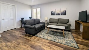 Ein Wohnzimmer mit zwei Sofas, einem Couchtisch, einer TV-Konsole und einem Fenster mit Jalousien.