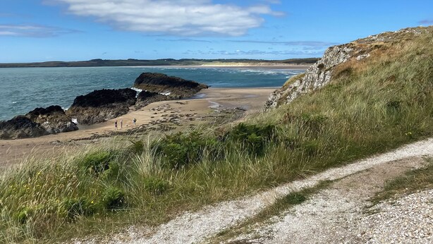 A coastal road with a gravel path leading to a beach with rocky outcrops and grassy areas. - Tyn Giat Cottage offers a perfect home for your relaxing getaways. (Amlwch and North Anglesey Heritage Coast)