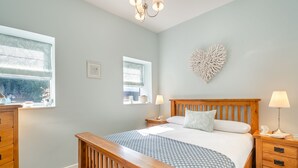 A bedroom with a wooden bed, bedside tables, a nightstand, a chandelier, and a window with a view. - Tyn Giat Cottage offers a perfect home for your relaxing getaways. (Amlwch and North Anglesey Heritage Coast)