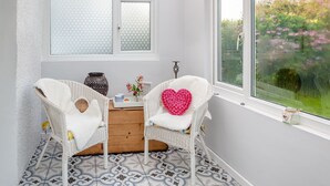 A room with two white wicker chairs, a small wooden table, and a window with frosted glass panes. - Tyn Giat Cottage offers a perfect home for your relaxing getaways. (Amlwch and North Anglesey Heritage Coast)