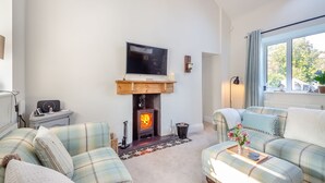 A cozy living room with a fireplace, a television, and a large window with a view of trees. - Tyn Giat Cottage offers a perfect home for your relaxing getaways. (Amlwch and North Anglesey Heritage Coast)