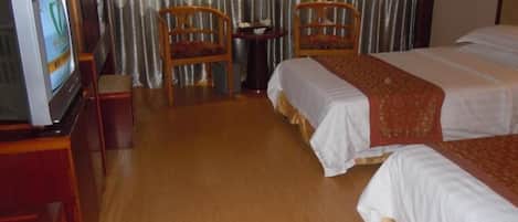 A hotel room with two beds, a television, and two wooden chairs.