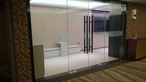 A modern hotel room with a glass partition, a small white desk, and a patterned carpet. - Gold Deer Hotel (Nan'an)