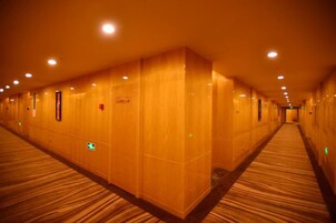 A hotel corridor with carpeted floors, wall-mounted light fixtures, and a long, straight layout.
