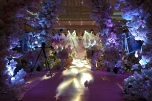 An indoor venue with a central aisle flanked by floral arrangements and lighting. - Gold Deer Hotel (Nan'an)