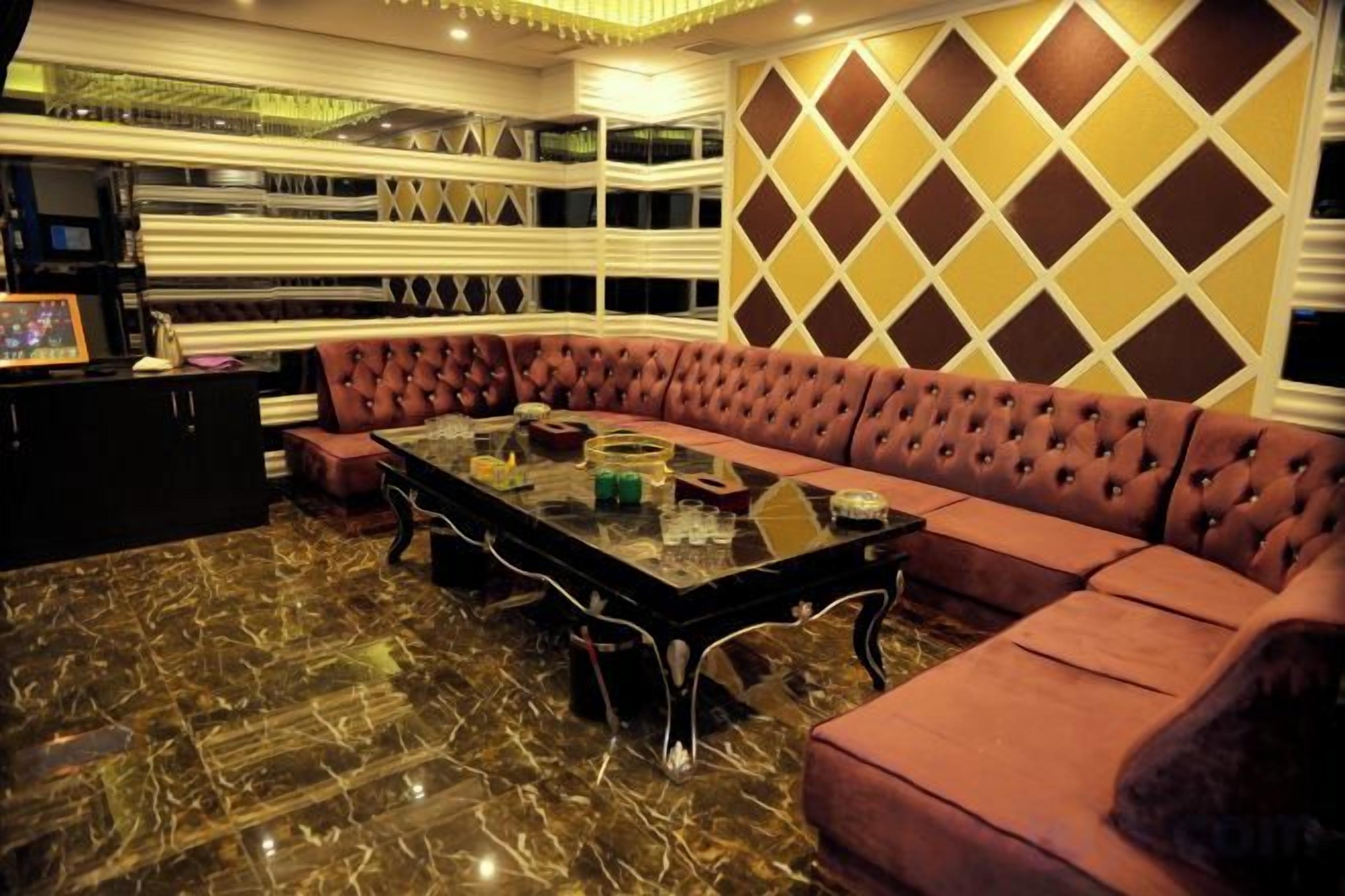 A room with a sectional sofa, a glass-top coffee table, and a patterned wall.