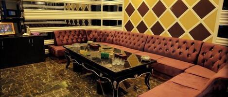 A room with a sectional sofa, a glass-top coffee table, and a patterned wall.