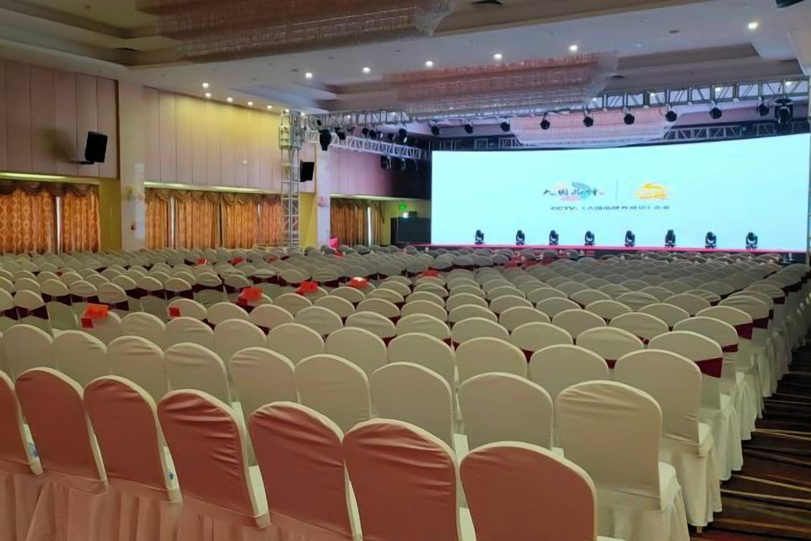 Uma sala de conferências com fileiras de cadeiras, um palco com uma tela e um pódio.