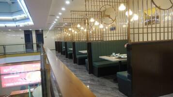 A restaurant with booths and a long counter, modern lighting fixtures, and a visible menu screen.