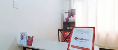 A hotel room with a table, a framed certificate, and a poster on the wall.