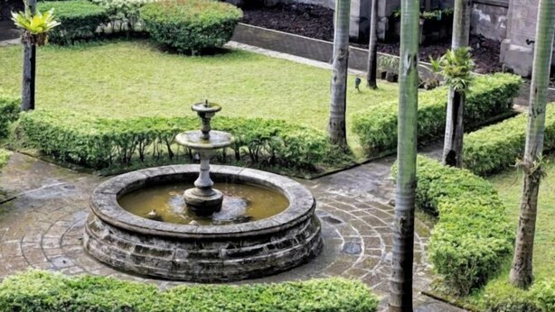A circular stone fountain with water in the center, surrounded by neatly trimmed hedges and palm trees. - RedDoorz Plus @ Remarkable Hotel Alcala Pangasinan (Pangasinan)