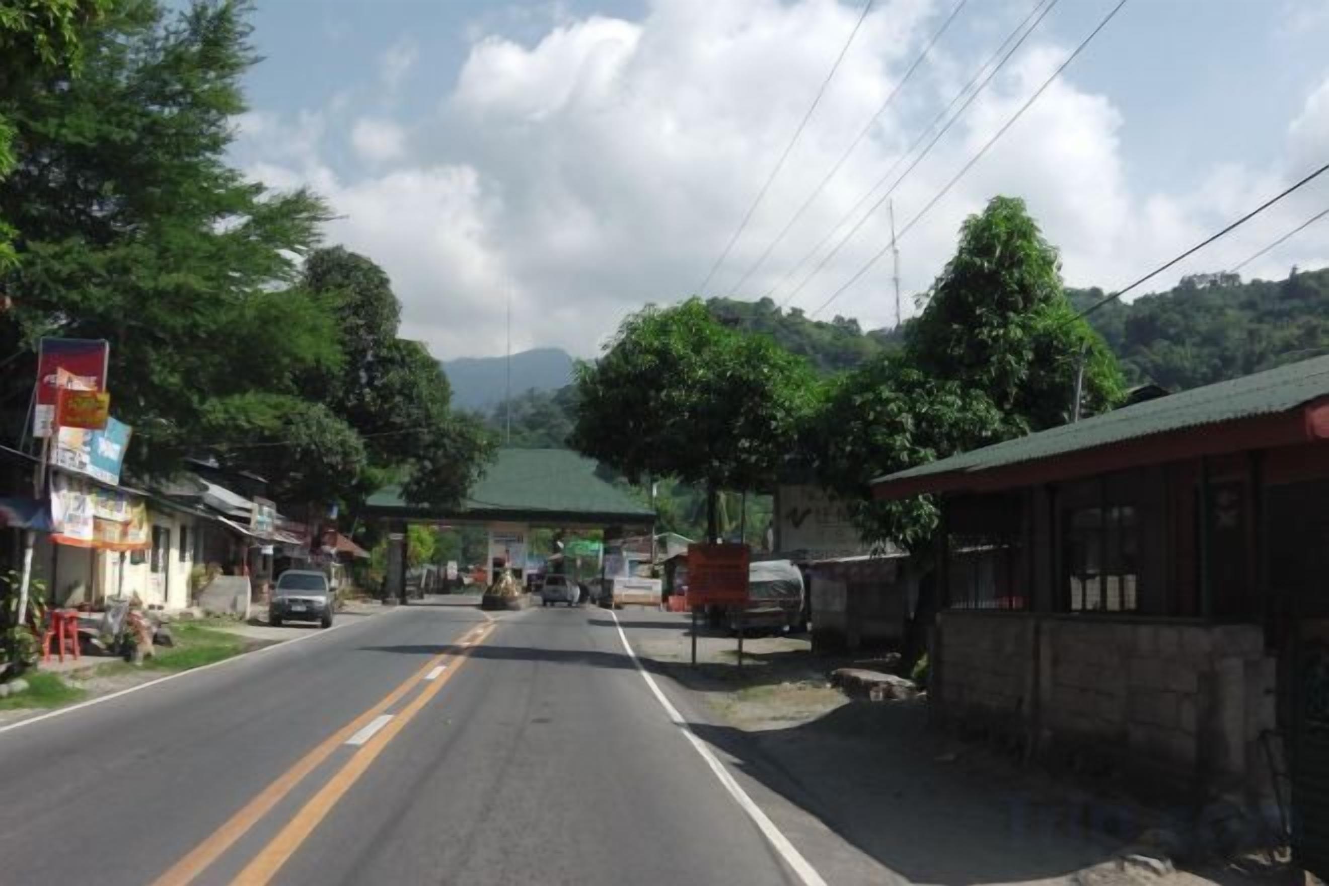 A road with buildings on the side, a gas station, and mountains in the background.