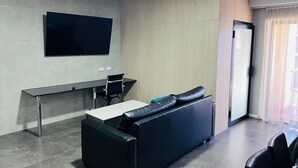 Una habitación de hotel moderna con una televisión de pantalla plana en la pared, un sofá, una mesita y un escritorio con una silla.