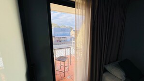 Una habitación con una cama, un ventanal con cortinas traslúcidas y vista a un edificio.
