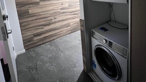 A compact laundry room with a built-in washer and dryer, wooden wall paneling, and a tiled floor. - One Bedroom Deluxe Spa Apartment (Hamilton)