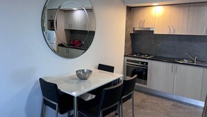 A compact kitchen with a round mirror, a dining table with chairs, and modern cabinetry. - One Bedroom Deluxe Spa Apartment (Hamilton)