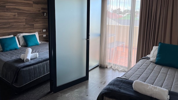 A hotel room with two beds, a sliding door, and a balcony with curtains. - One Bedroom Deluxe Spa Apartment (Hamilton)