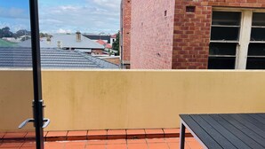 Ein Balkon mit Fliesenboden, einem schwarzen Tisch und einer gelben Wand.
