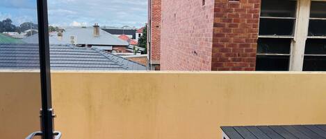 A balcony with a tiled floor, a black table, and a yellow wall.
