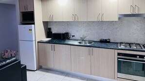Eine kleine Küche mit hellen Holzschränken, einer eingebauten Mikrowelle, einem Toaster, einem Wasserkocher, einer Spüle und einem Geschirrspüler.