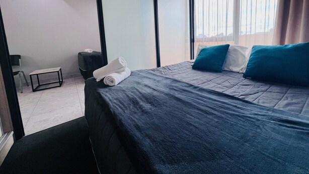 Ein Hotelzimmer mit Bett, einem kleinen Tisch, einem Sessel und einem Fenster mit Vorhängen.