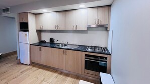 Une cuisine moderne avec des meubles de couleur bois clair, un plan de travail noir, un évier en acier inoxydable, une cuisinière à gaz et un four encastré.