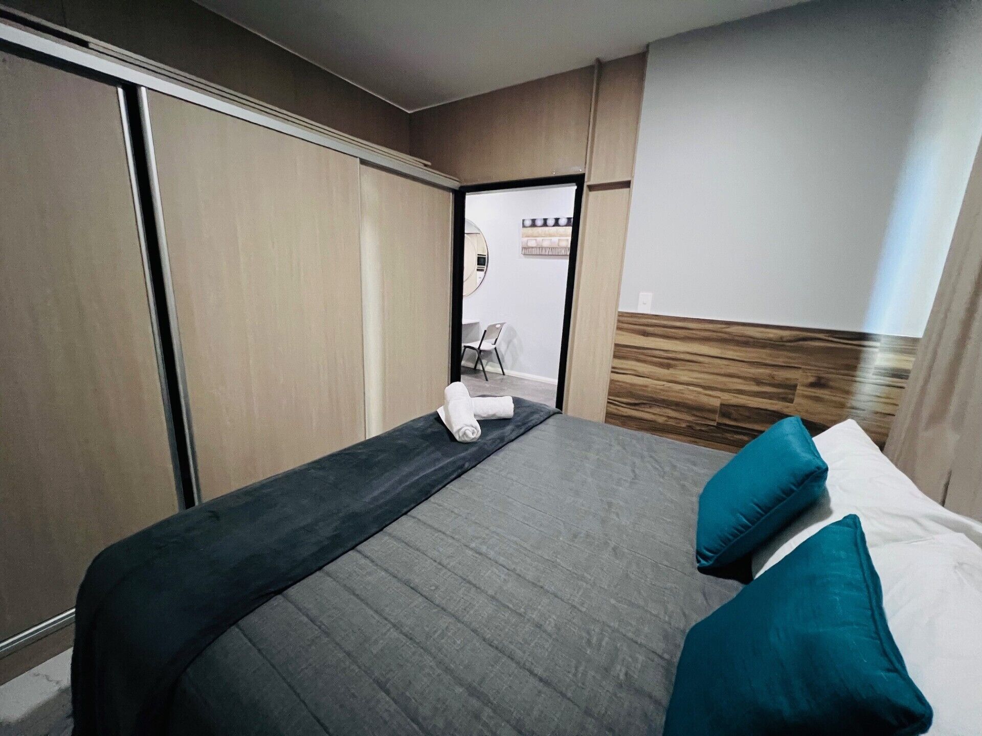 Une chambre d’hôtel avec un lit, une tête de lit en bois, un miroir et une vue sur la salle de bain.