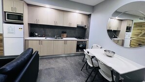 Une cuisine moderne avec des meubles en bois clair, un plan de travail blanc, un évier, une cuisinière et un coin repas comprenant une table et des chaises blanches.