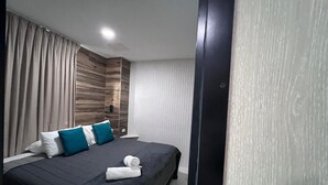 Une chambre d’hôtel moderne avec un grand lit, une literie aux couleurs sombres et des oreillers turquoise.