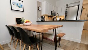 A modern kitchen with white cabinets, a stainless steel refrigerator, and a wooden dining table with black chairs. - 2BR 2BA Village Escape w/ Updated Hot Tub, Perfect Location & Mountain Views (Whistler)