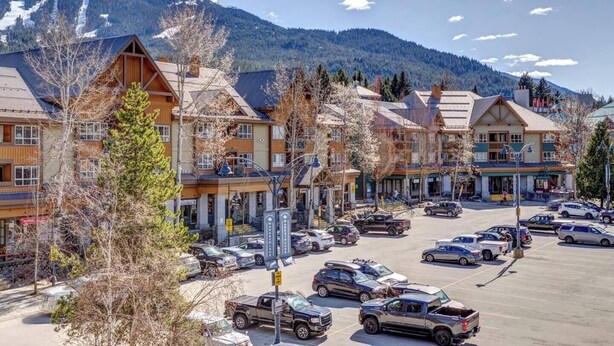 A mountain resort with multiple-story buildings, a parking lot, and a view of snow-capped mountains. - 2BR 2BA Village Escape w/ Updated Hot Tub, Perfect Location & Mountain Views (Whistler)