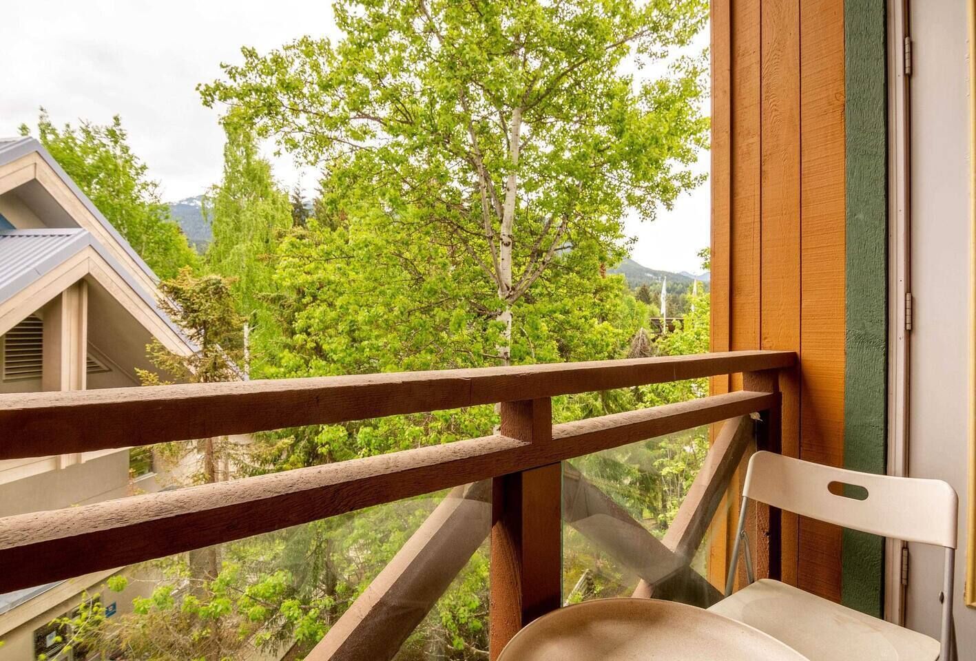 A balcony with a wooden railing overlooking a lush green landscape and a mountain in the distance.