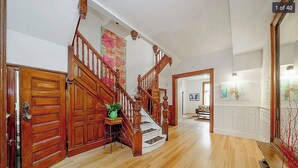 Un pasillo espacioso con suelo de madera, una imponente escalera y una gran puerta de madera.