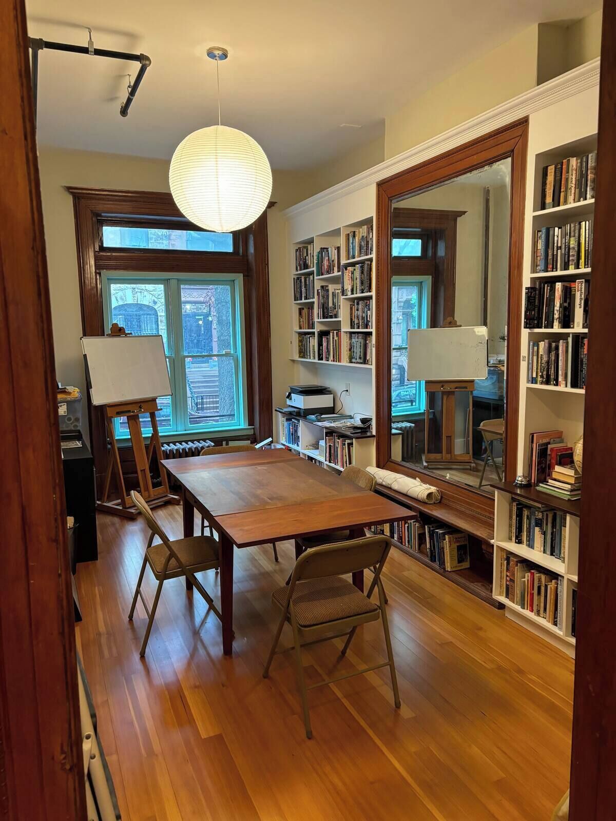 Une pièce avec une table en bois, deux chaises, un grand miroir et des étagères remplies de livres.