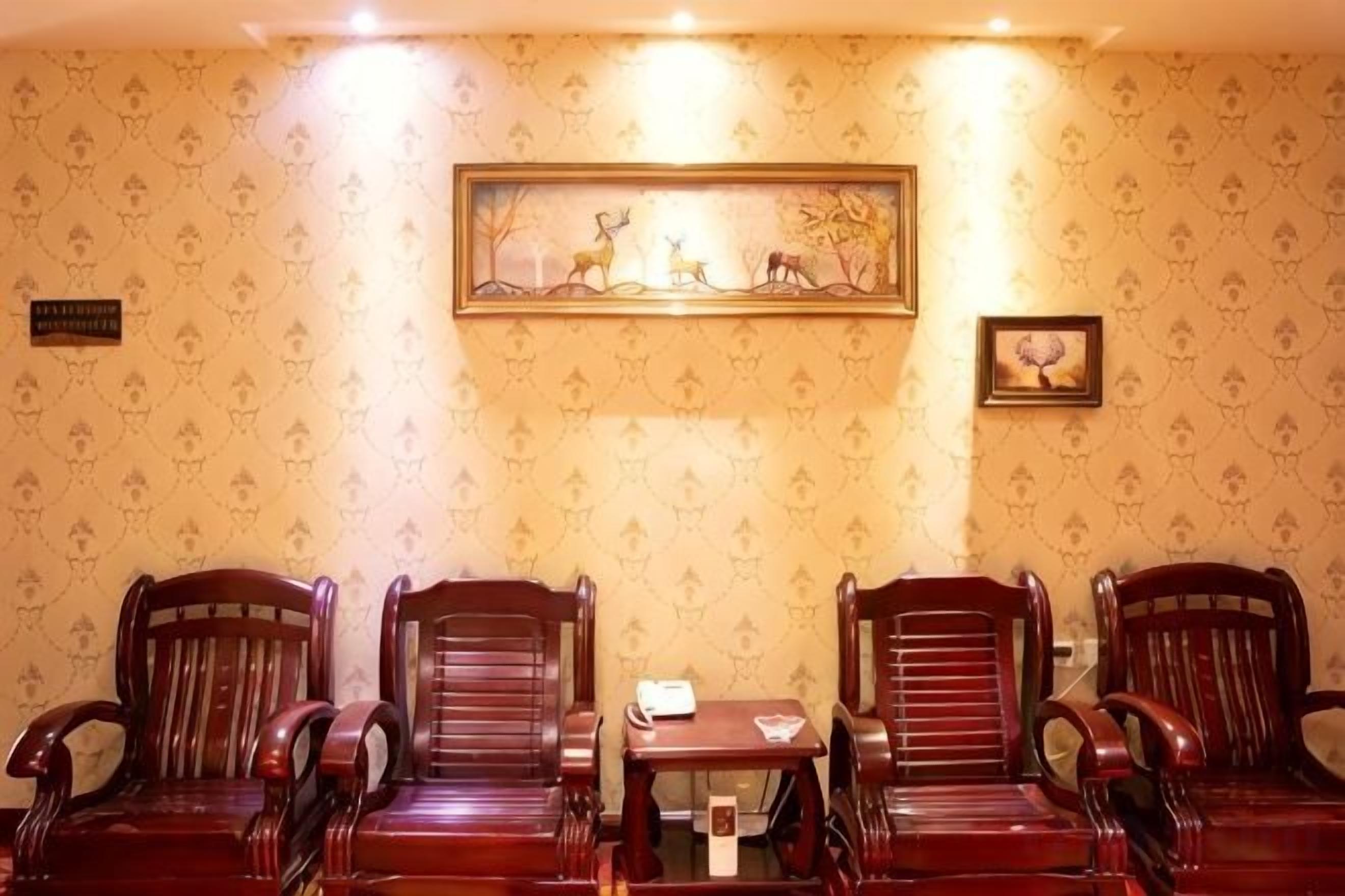 A room with four wooden chairs and a small table, a framed picture on the wall, and a sign indicating a room number.
