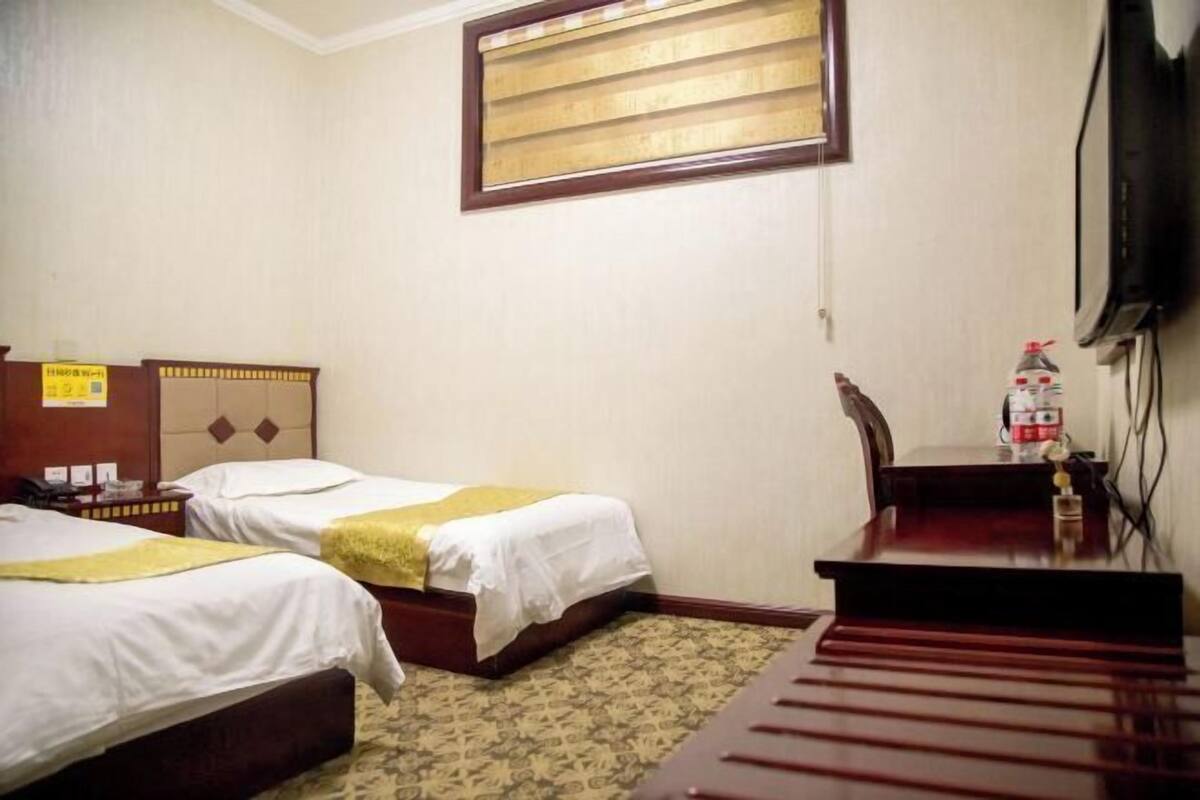 A hotel room with two beds, a desk, a chair, a television, and a window with blinds.