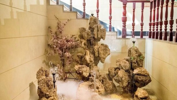 Um jardim rochoso com fonte de água e escadaria com balaústres vermelhos.