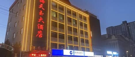A multi-story hotel with a prominent sign, a storefront with a blue sign, and a street view with cars.