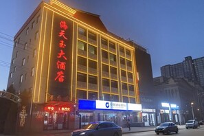 A multi-story hotel with a prominent sign, a storefront with a blue sign, and a street view with cars. - Qingxu Haitianyu Hotel (Qingxu)