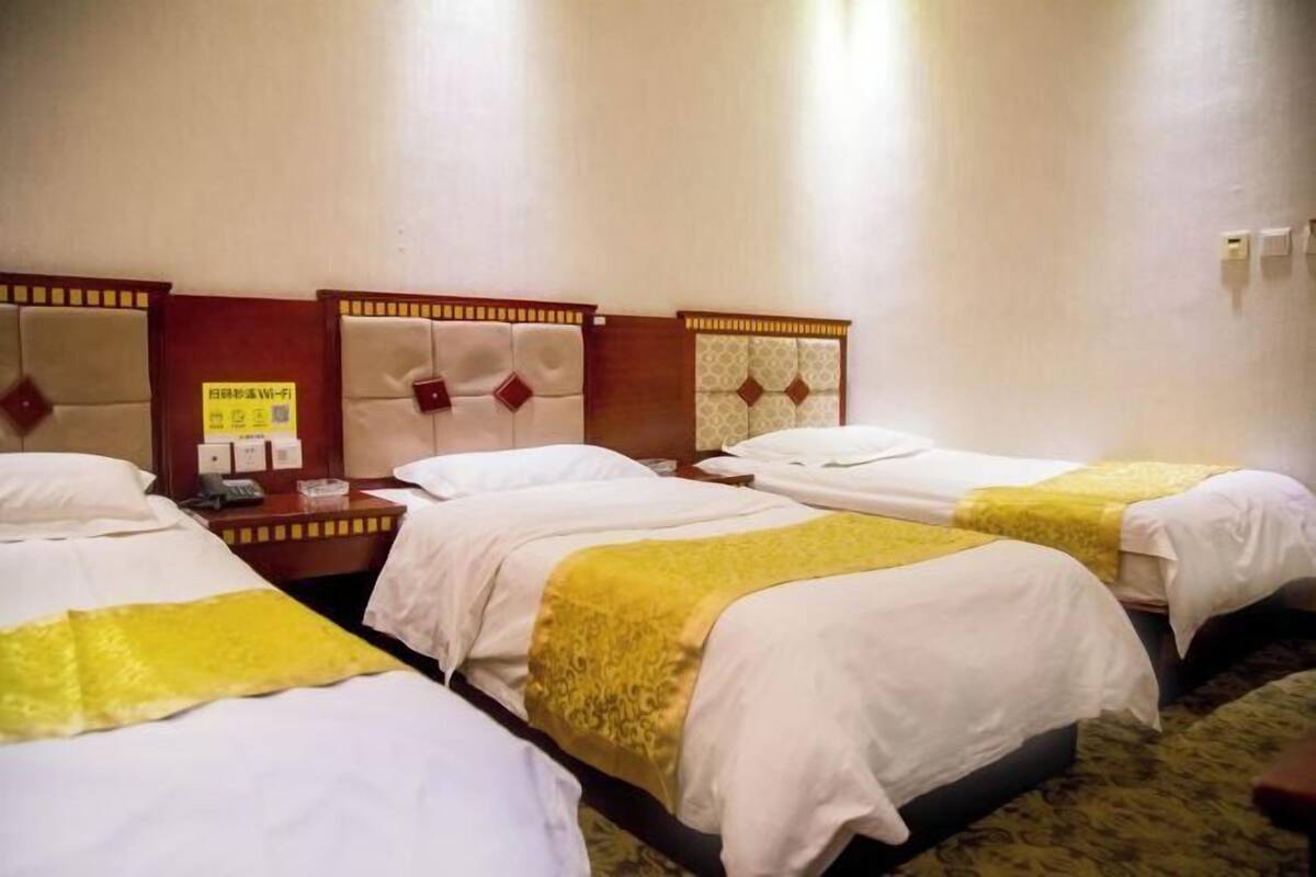 A hotel room with three beds, each with a headboard and a bedside table.