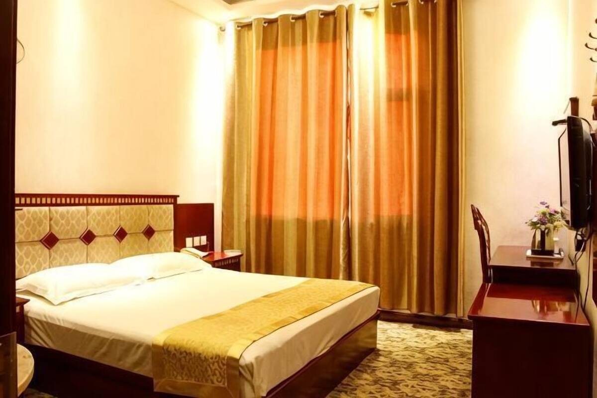 A hotel room with a bed, a desk, a chair, a TV, and a window with curtains.