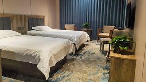 Quarto de hotel com duas camas, uma televisão, uma mesinha com uma planta e uma cadeira.