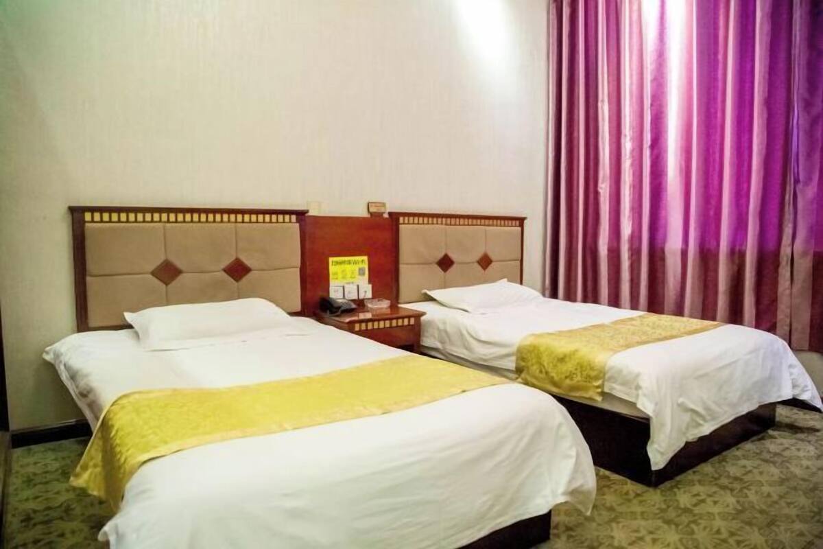 A hotel room with two beds, a wooden headboard, a nightstand, and a window with curtains.