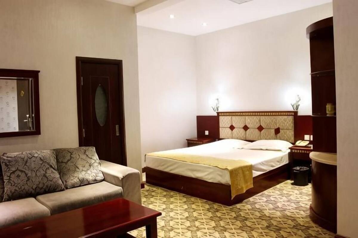 A hotel room with a bed, a sofa, a bedside table, and a mirror.