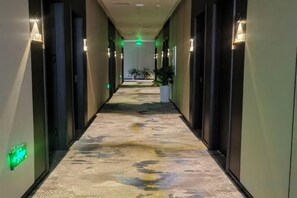 A hotel hallway with a patterned carpet, wall sconces, and a green exit sign. - Qingxu Haitianyu Hotel (Qingxu)